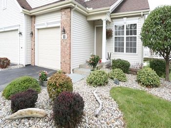 Exterior of townhome with attached 1-car garage rock garden with driftwood and plantings and private, covered front porch